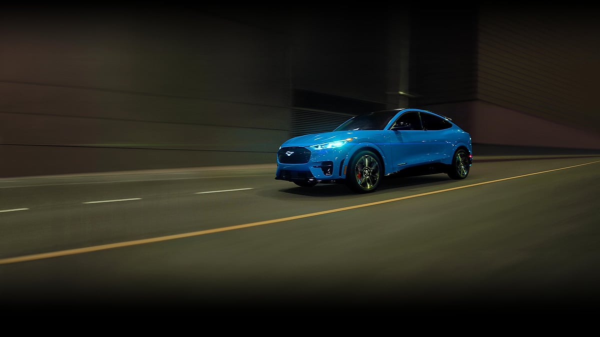 Blue Ford Mustang Mach-E driving at night with its headlights on.