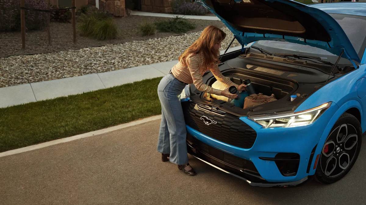 Woman loading items into the front trunk (frunk) of a blue Ford Mustang Mach-E GT electric SUV.