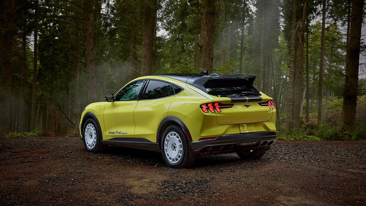 Yellow Ford Mustang Mach-E Rally parked on a forest road in a rear three-quarter view.