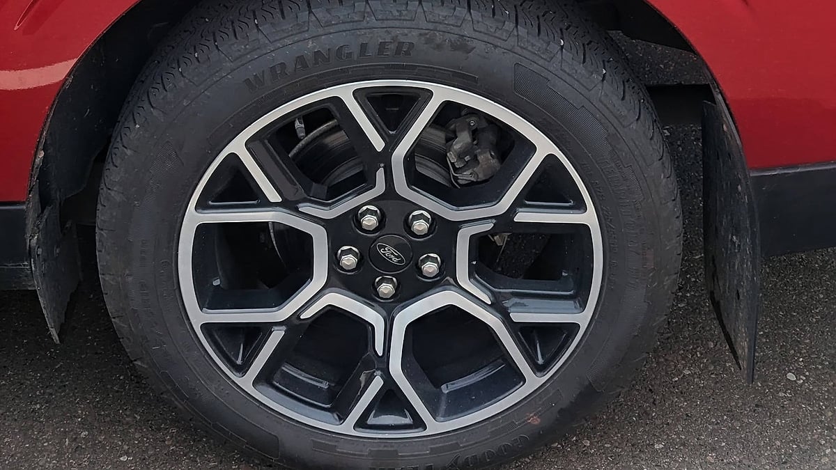 Close-up of a Ford alloy wheel fitted with a Goodyear Wrangler tire beneath a red body panel.