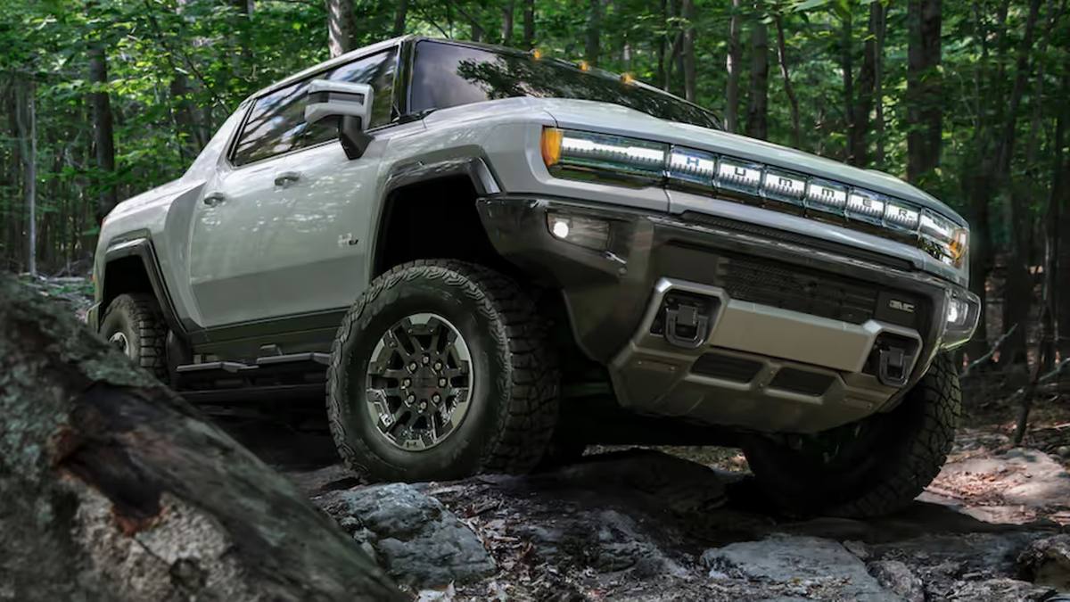 GMC Hummer EV white electric SUV driving on forest trail with evergreen trees