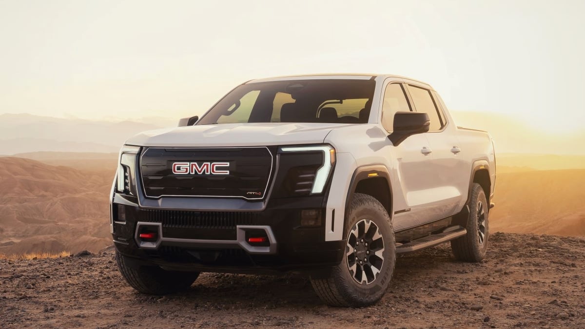 White GMC Sierra EV AT4 pickup truck parked on a desert overlook at sunset, front three-quarter view