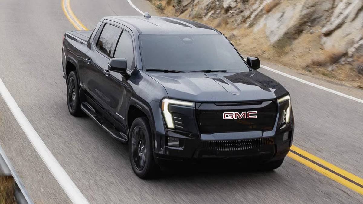 GMC Sierra EV black electric truck on mountain highway with motion blur and scenic landscape