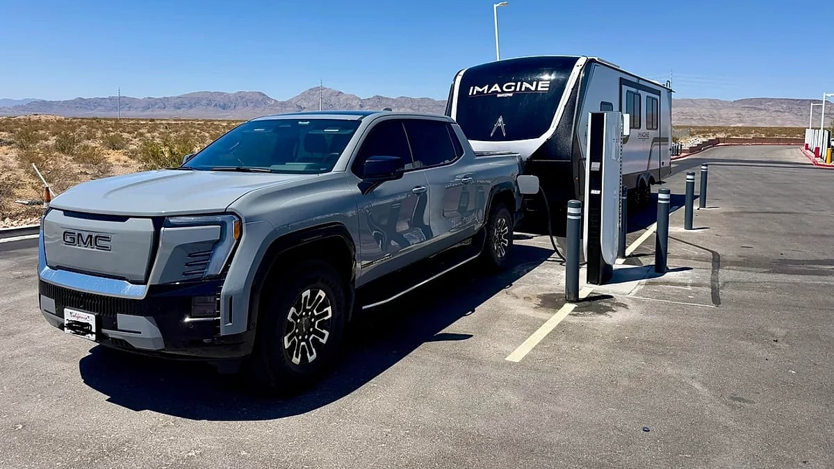 GMC Sierra EV towing an Imagine travel trailer through a desert landscape surrounded by red rock formations