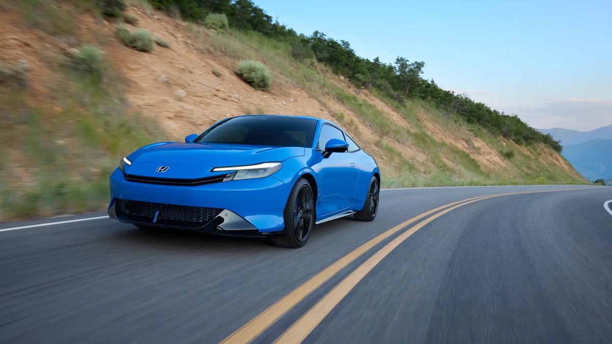 Blue Honda Prelude driving on a winding mountain highway on a sunny day