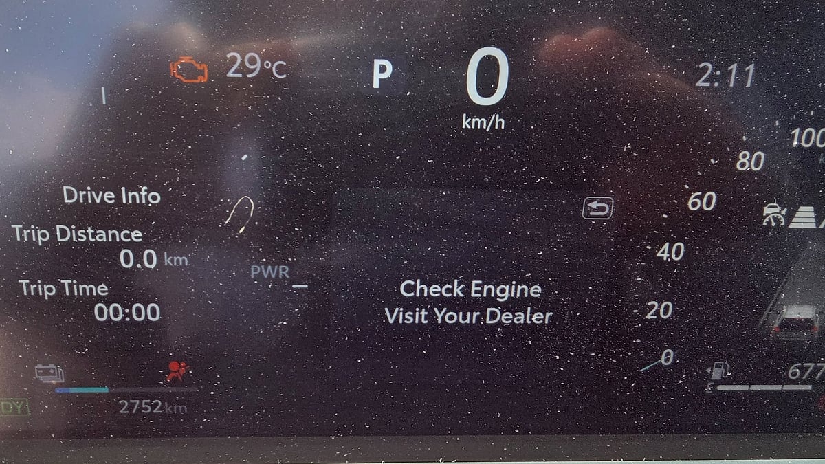 Close-up of a vehicle instrument cluster displaying a "Check Engine, Visit Your Dealer" warning