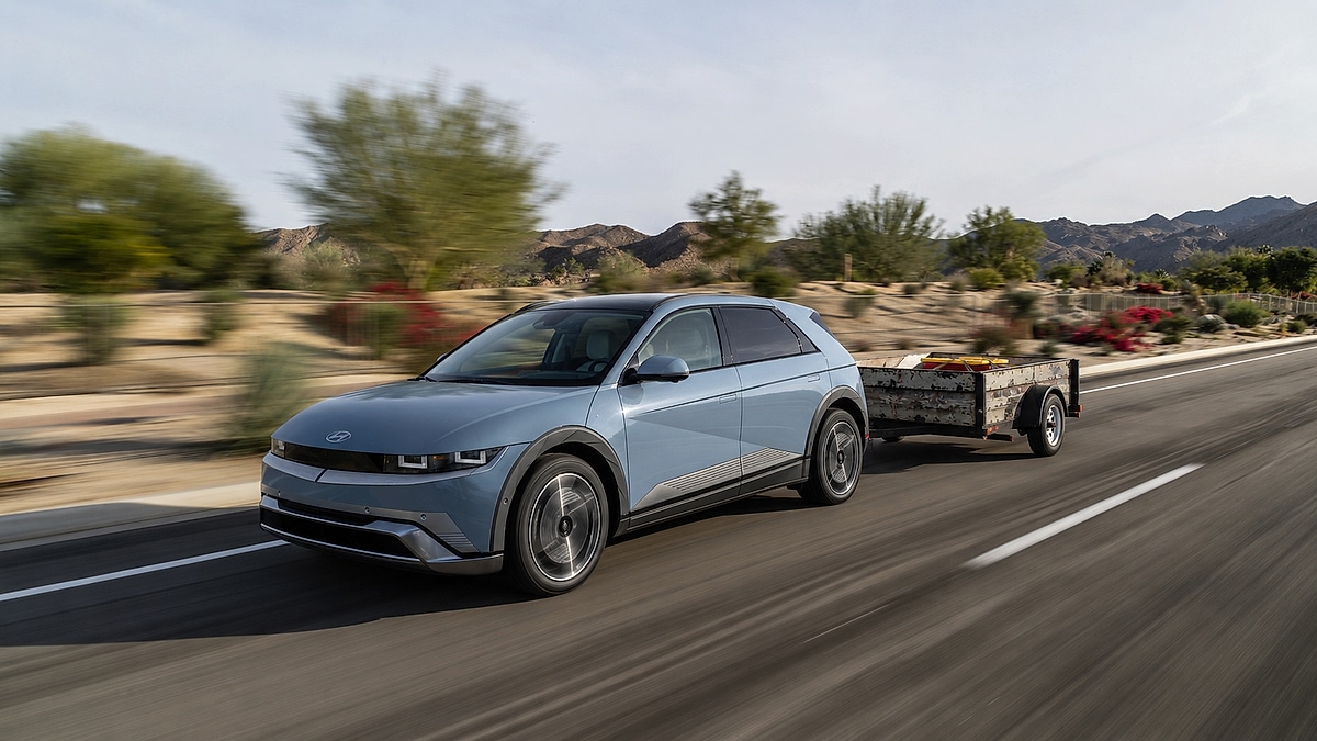 Hyundai Ioniq 5 towing a small utility trailer on a desert road with mountains in the background.