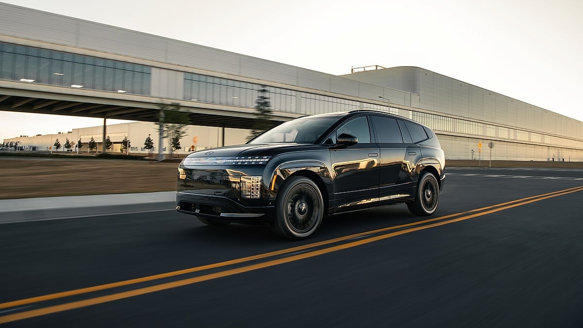 Black Hyundai IONIQ 9 driving under a modern building with glass walkways and motion blur.