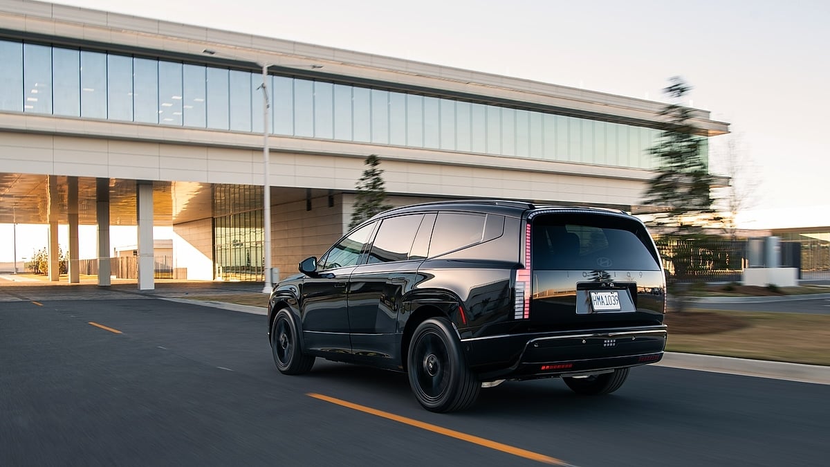Rear three-quarter view of a black Hyundai Ioniq 9 driving past a modern building at dusk.