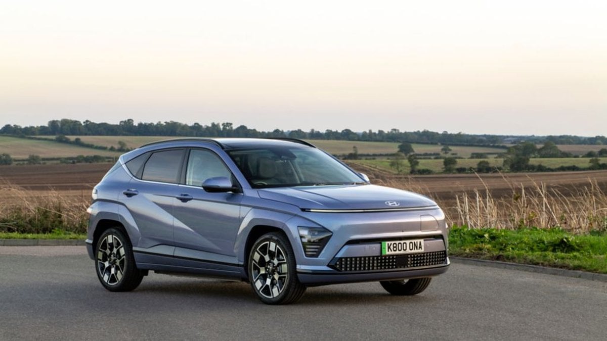 Grey Hyundai Kona Electric parked on pavement with trees in the background, showing a full side profile of the compact electric SUV.