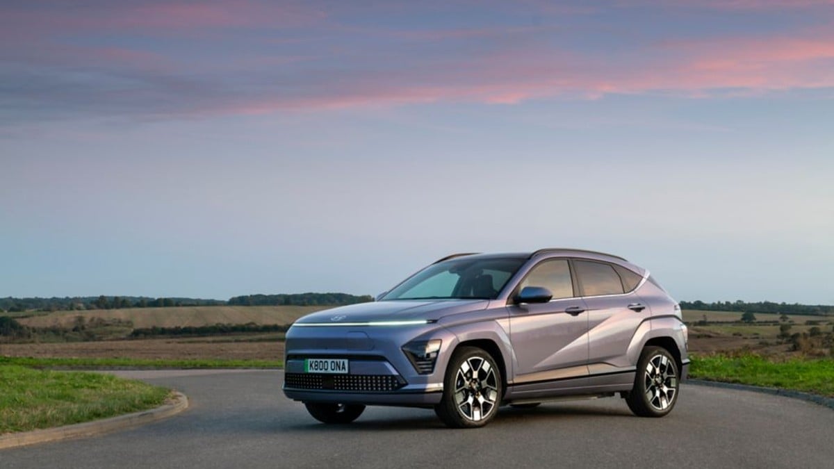 Grey Hyundai Kona Electric parked on a country road with open fields in the background, showing a side profile view.