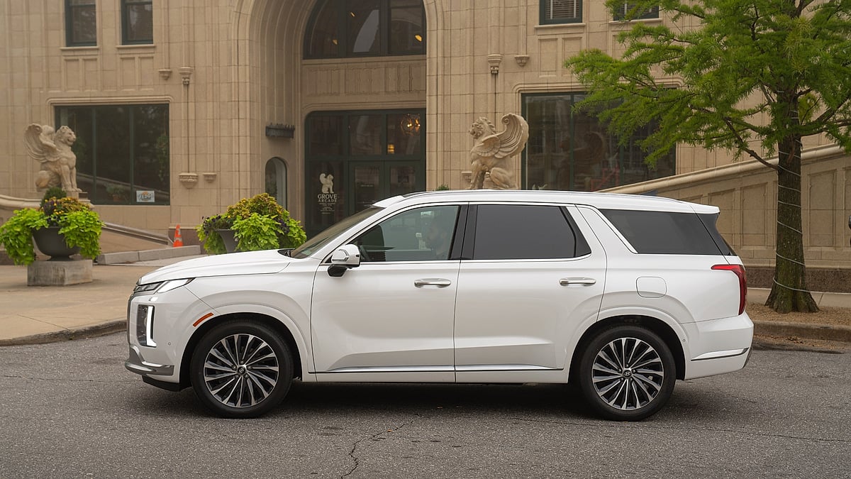 White Hyundai Palisade shown in side profile on an urban street outside a building.