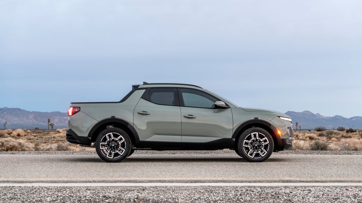 Sage green Hyundai Santa Cruz pickup parked on a desert road, side profile view with mountains in the background