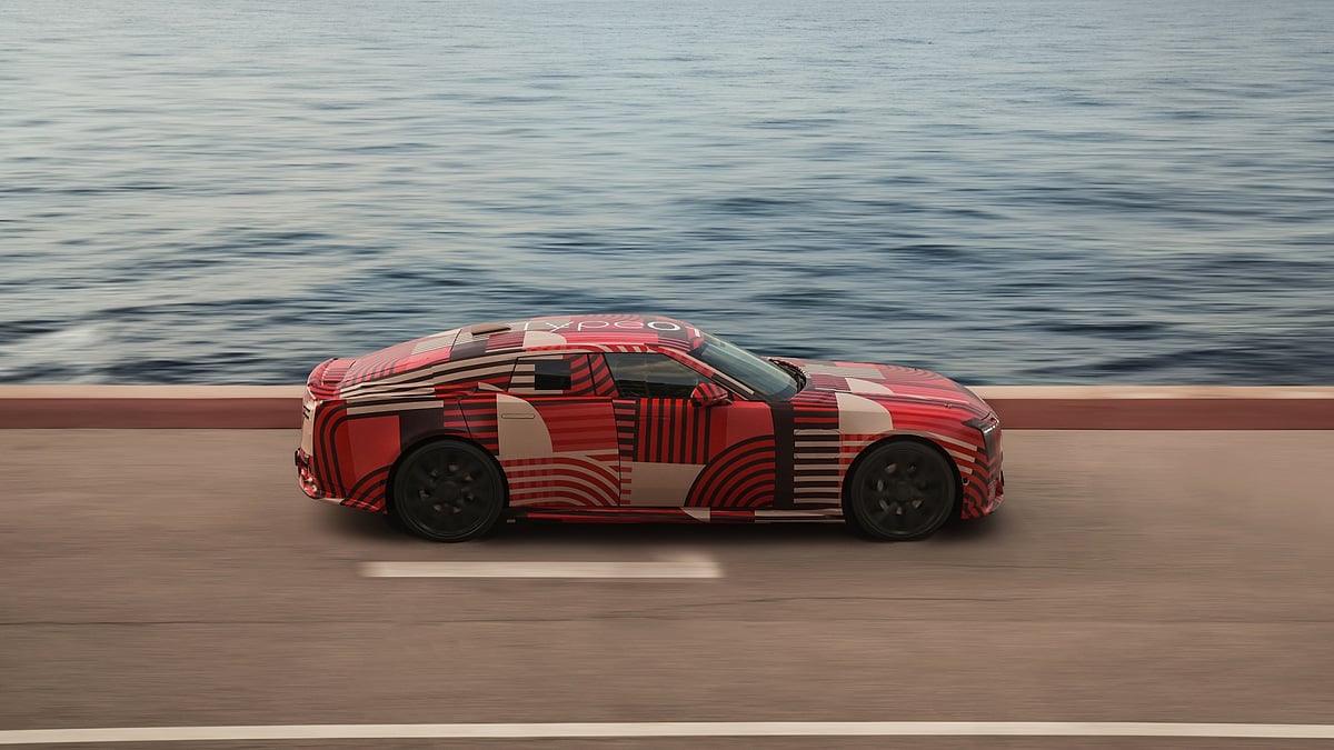 Camouflaged Jaguar Type 001 prototype driving along a coastal road in a side-profile view.