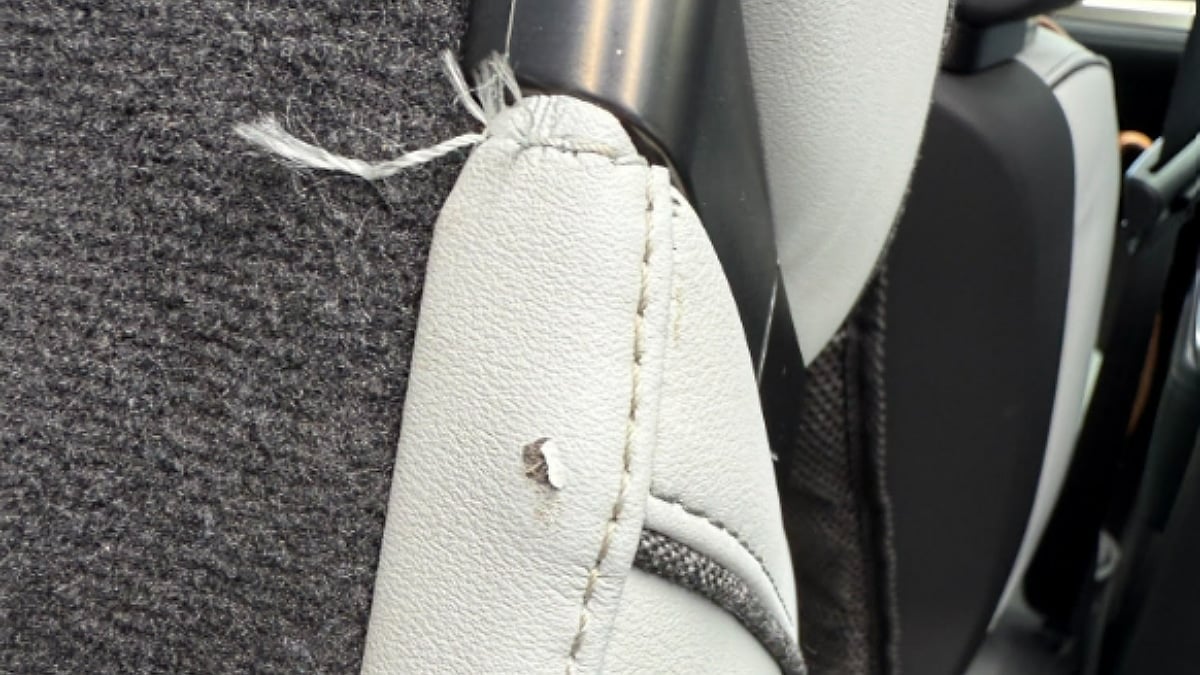 Close-up of a seat edge inside Kate's 2023 Rivian R1S showing a small tear near a stitched seam with loose fibers protruding from the damaged upholstery material.