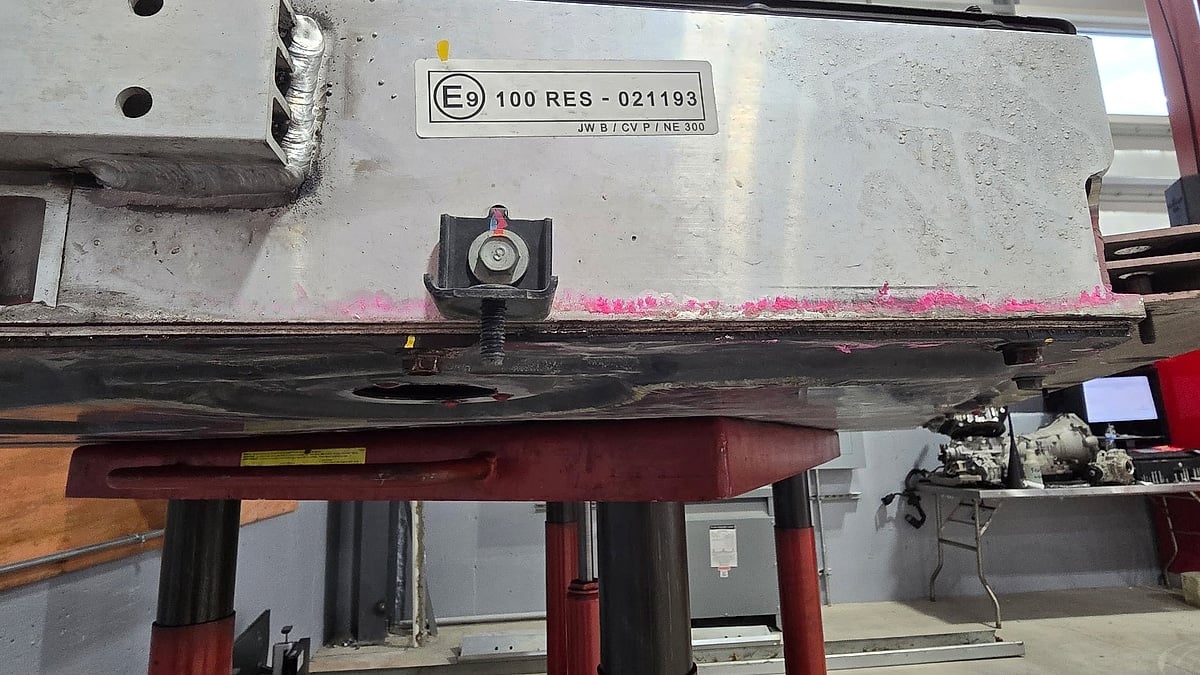 Close-up of the underside of a Kia EV6 battery pack on a lift, showing scrape marks and the area identified as damaged.