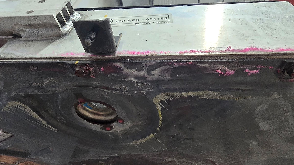 Close-up of the underside of a Kia EV6 battery pack on a lift, showing scuffs, mounting hardware, and the suspected impact area.