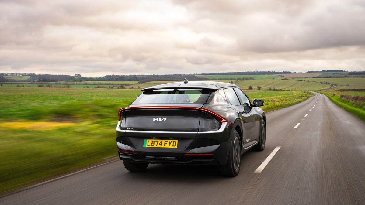 Rear view of a Kia EV6 electric car driving along a winding rural road through green countryside.