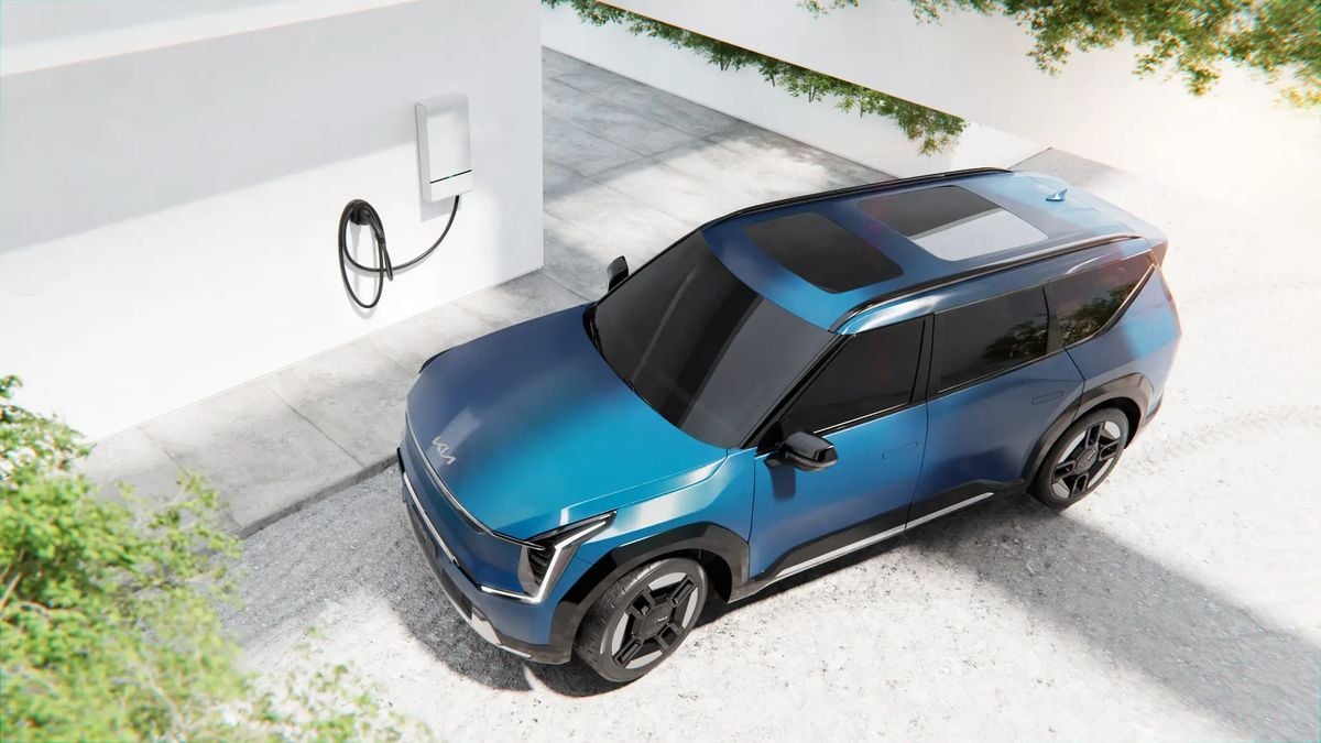 Blue Kia EV9 electric SUV charging at a home wallbox station, illustrating residential EV charging and sustainable transportation.