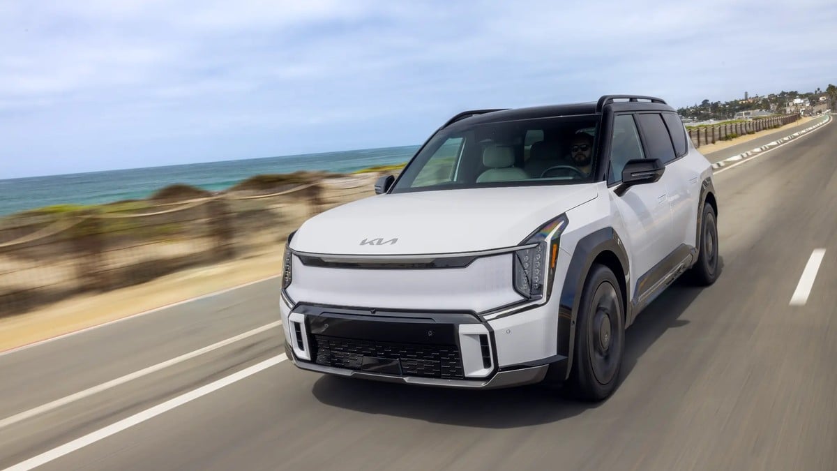 White Kia EV9 three-row electric SUV driving on coastal highway with ocean view
