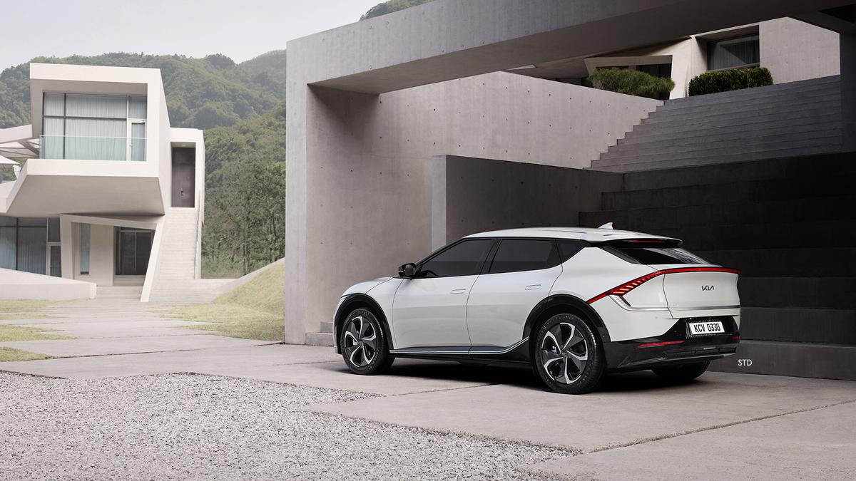 White Kia EV6 electric SUV parked outside modern concrete house, rear three-quarter view