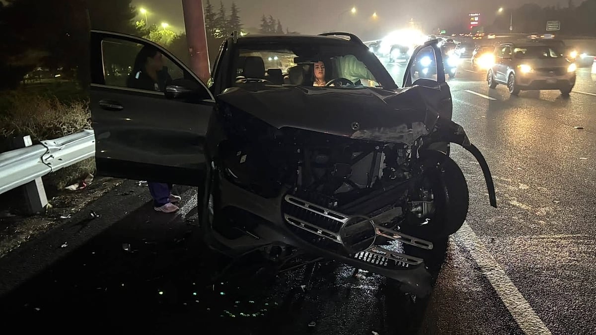 Laura’s Mercedes GLE 450e with significant front-end damage at the scene of a nighttime crash on a busy highway.
