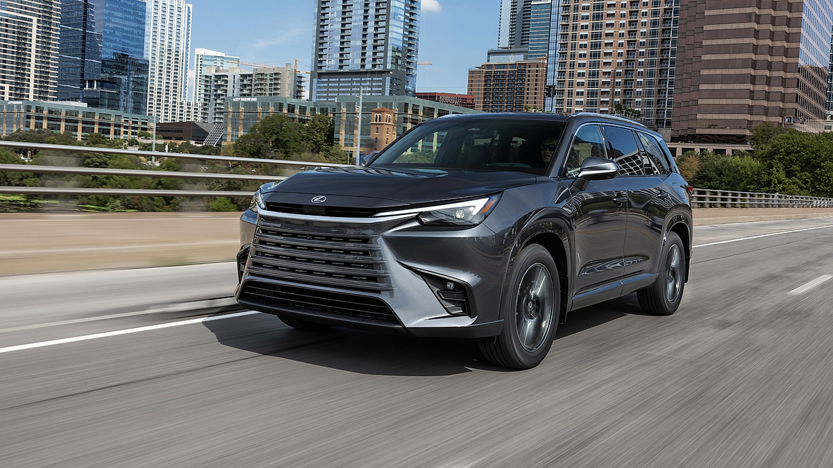 Gray Lexus TX SUV driving through city with skyline in background