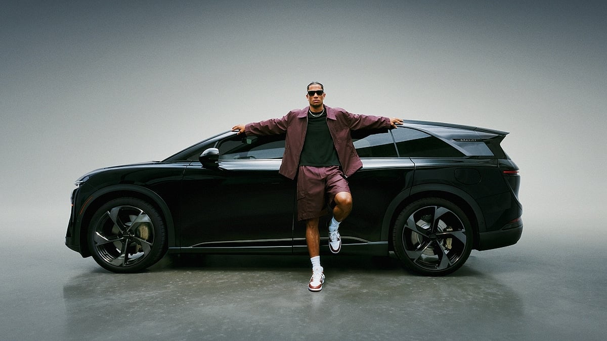 Side view of a black Lucid Gravity SUV in a studio with a person leaning against the vehicle.