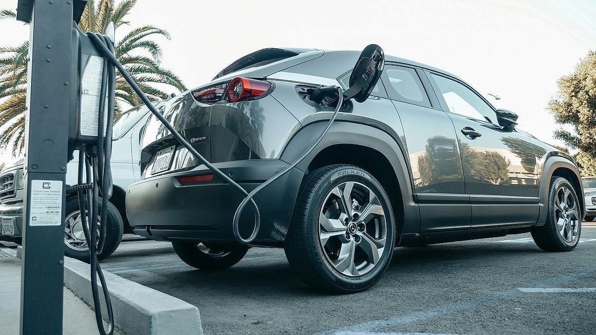 Gray Mazda MX-30 electric SUV plugged into a ChargePoint EV charging station in a sunny parking lot with palm trees