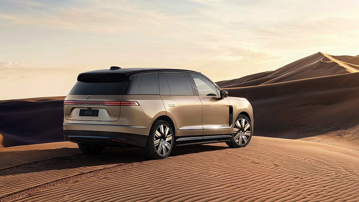 Gold Nio ES9 SUV shown from the rear three-quarter angle among desert dunes at sunset.