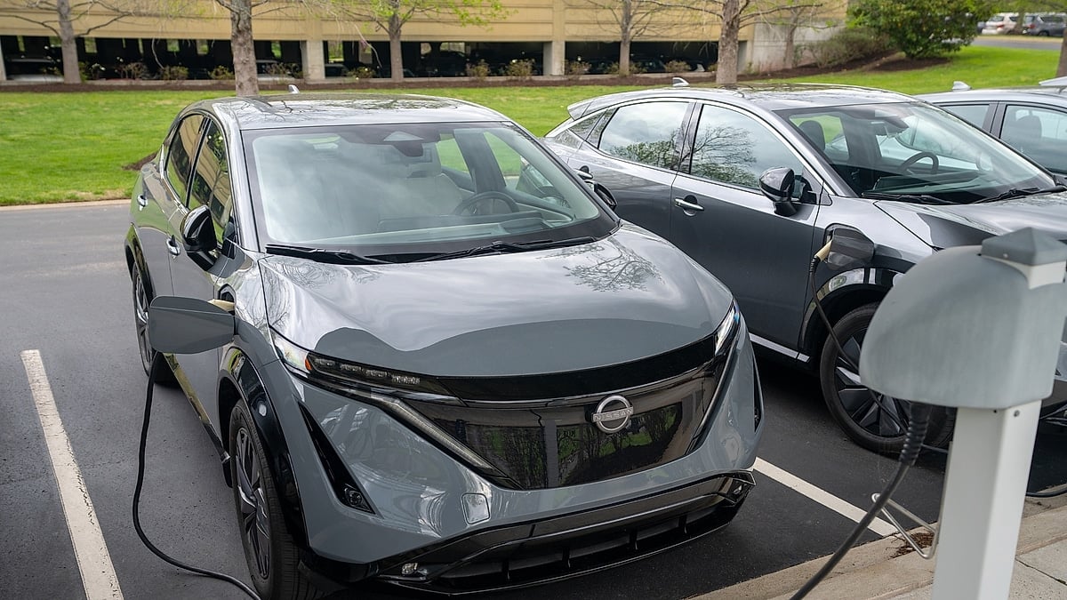 Two Nissan Ariya electric SUVs parked at charging stations in a public parking lot.