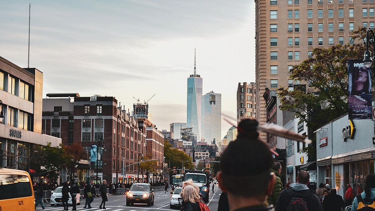Busy New York City street scene with traffic, pedestrians, and One World Trade Center in the distance.