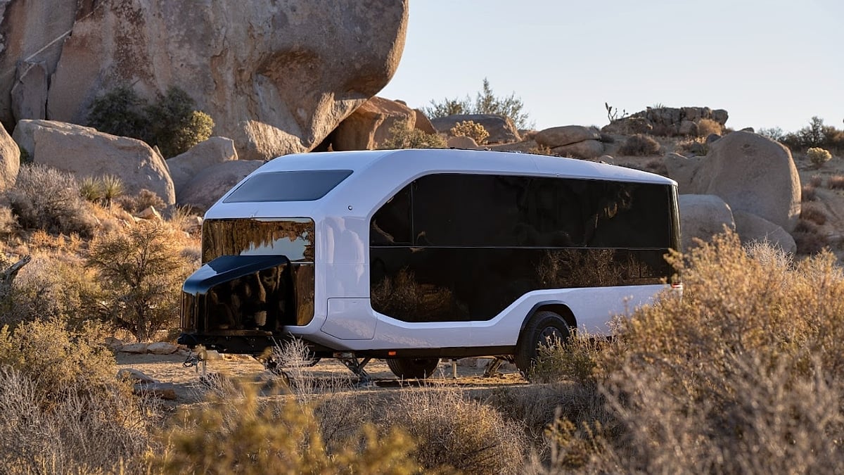 White Pebble Flow travel trailer parked among desert rocks in a side view.