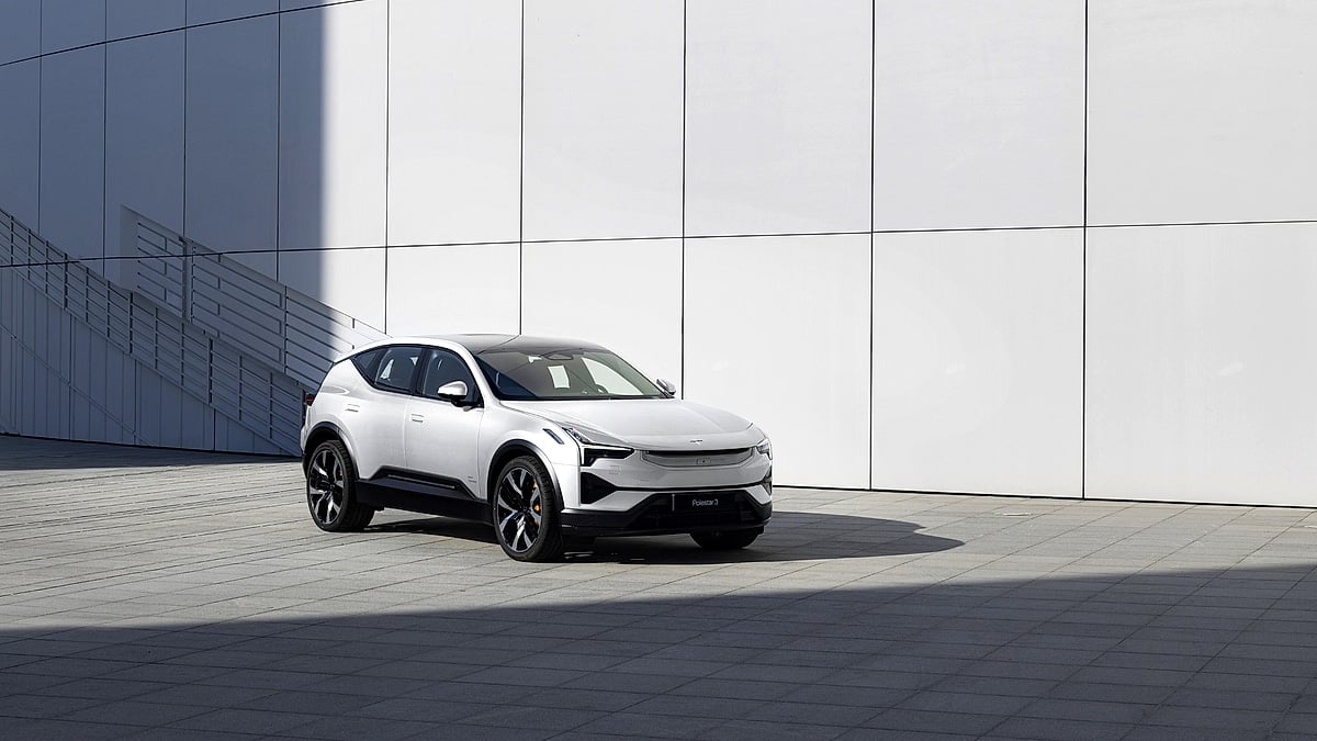 White Polestar 3 electric SUV parked on plaza in front of minimalist white panel wall in bright sunlight, front three-quarter view
