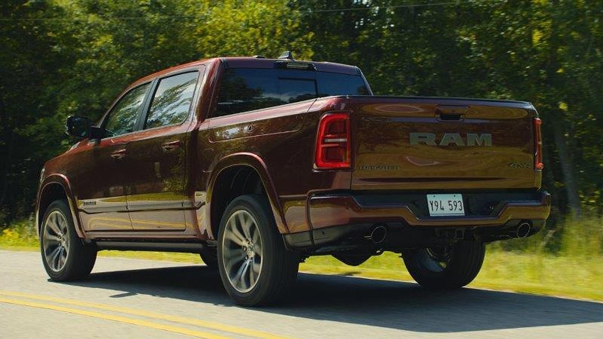 Dark red Ram 1500 pickup truck driving on a forest road, rear three-quarter view