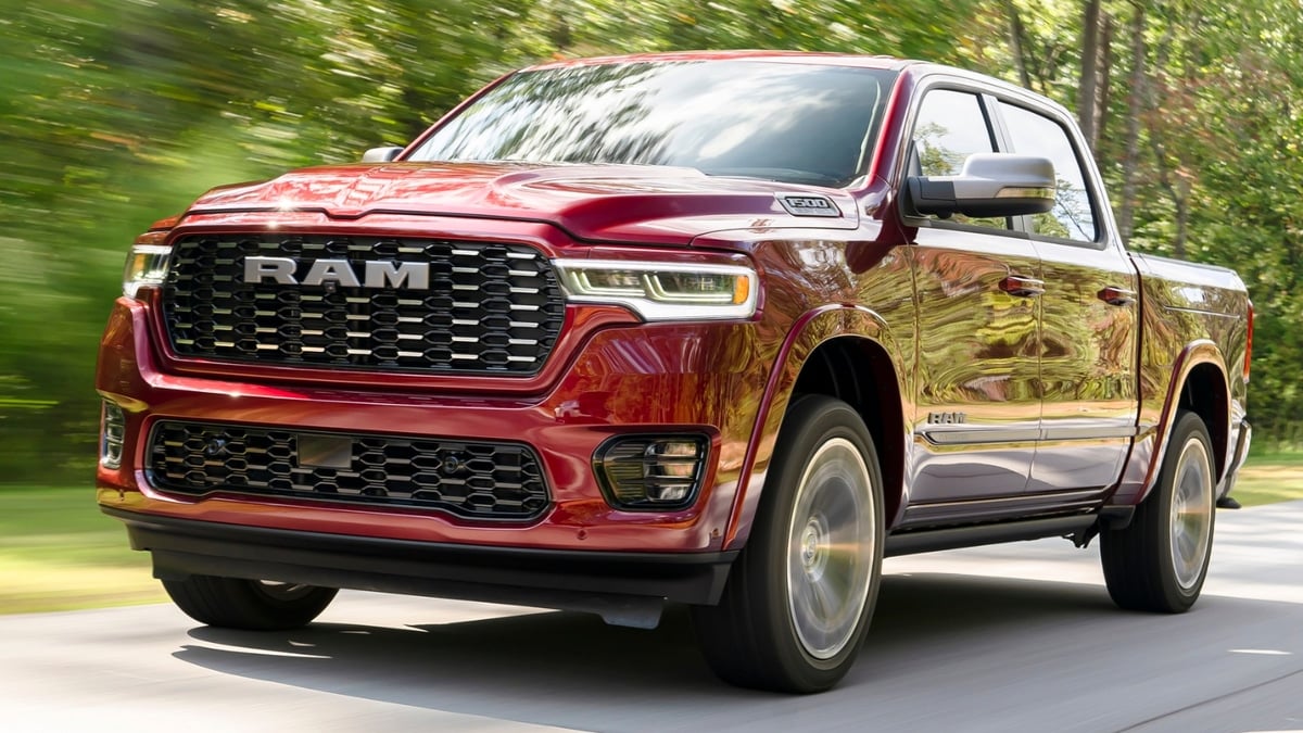 "Red Ram 1500 pickup truck driving down a tree-lined road, front three-quarter view with motion blur in the background