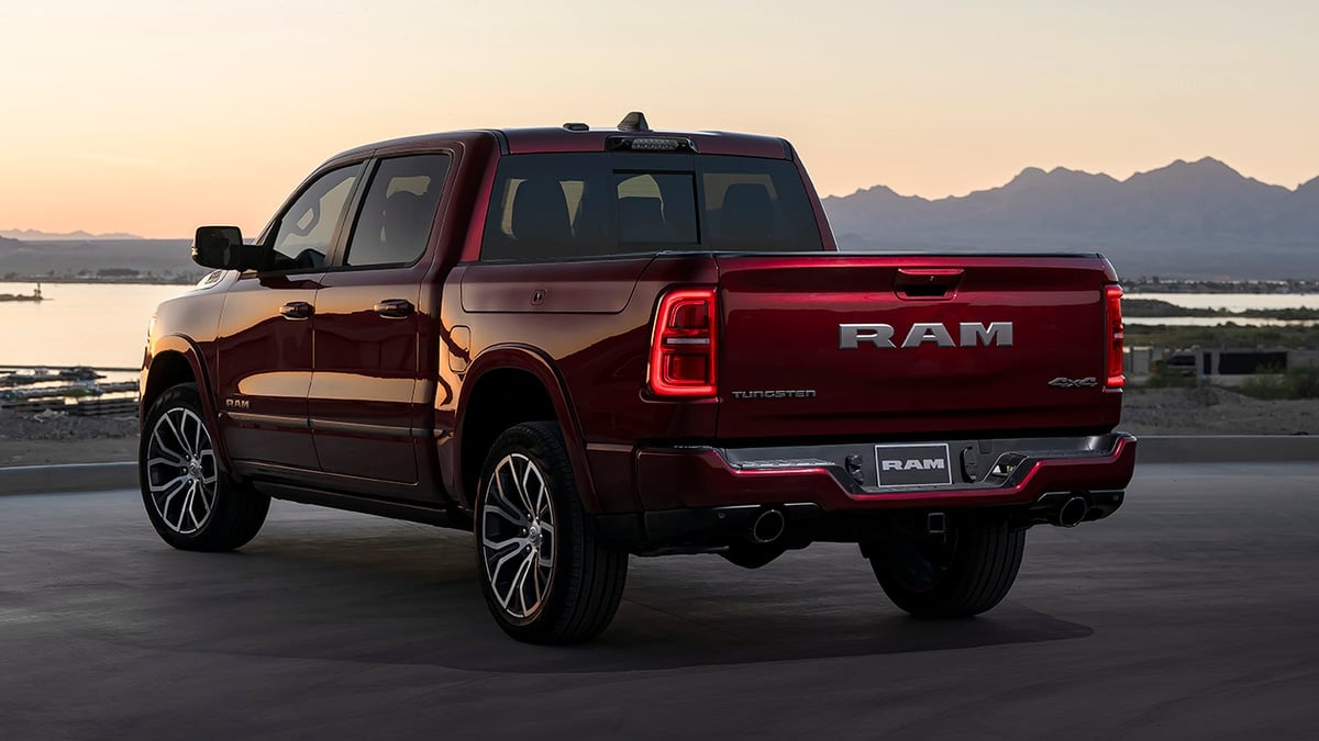 Red Ram 1500 Tungsten pickup truck parked overlooking a lake at sunset, rear three-quarter view with mountains in the distance