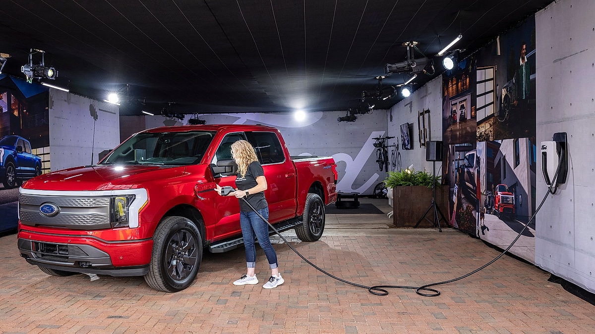 Red Ford F-150 Lightning being charged indoors at a branded display setup.