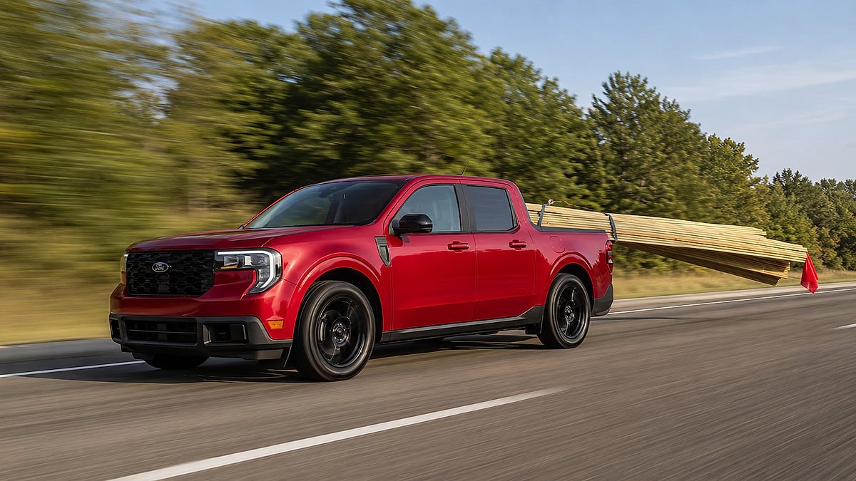 Red Ford Maverick hauling long lumber in the truck bed while driving on a highway.