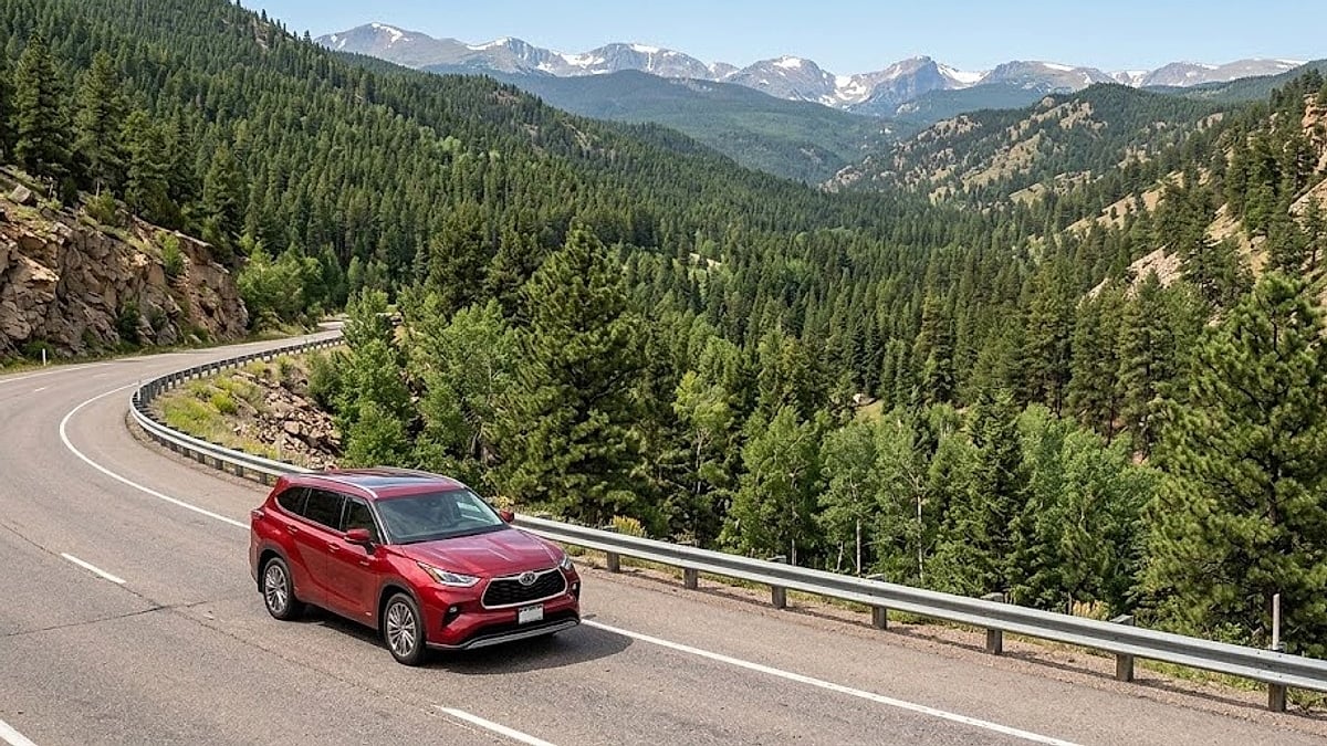 Red Toyota Highlander driving on winding mountain highway with pine trees and snow-capped Rocky Mountains