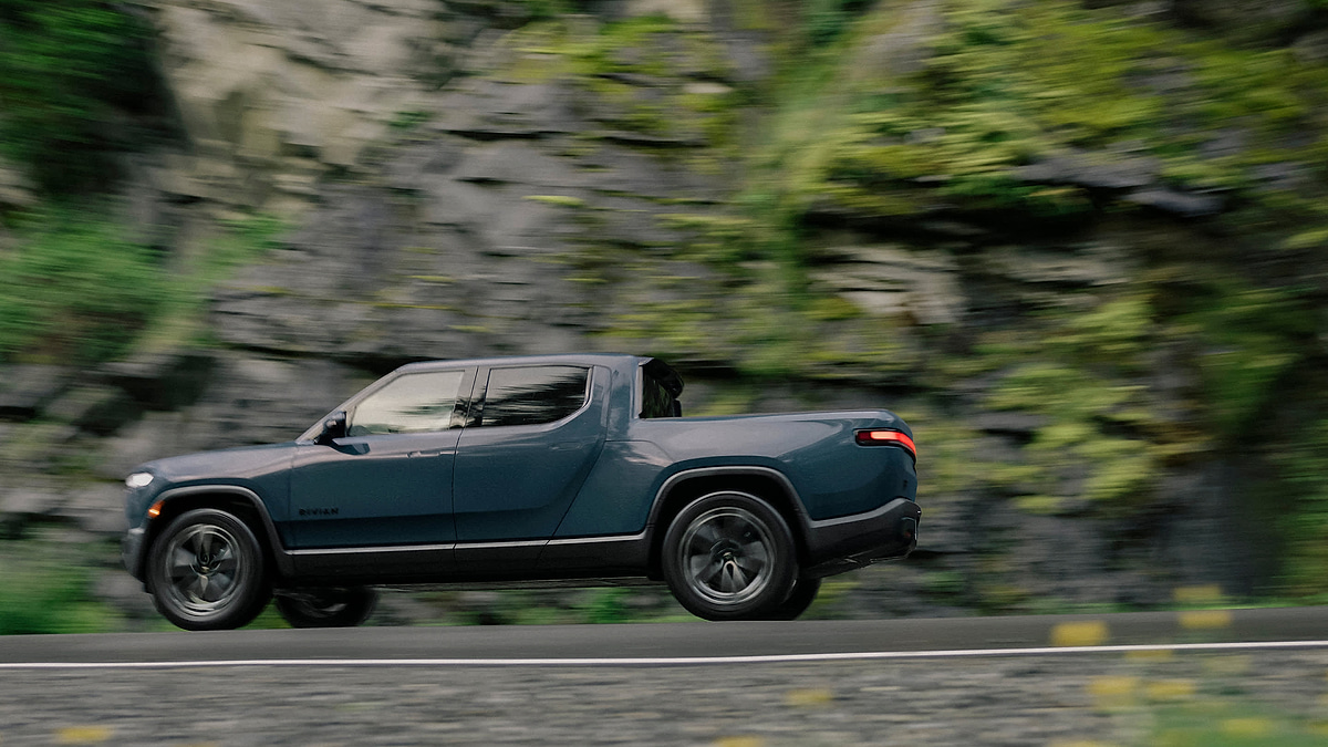 Rivian R1T side view driving through forest road