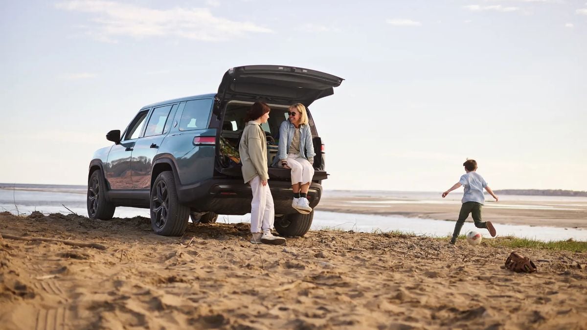 Rivian R1S electric SUV parked on the beach with family standing by the open tailgate