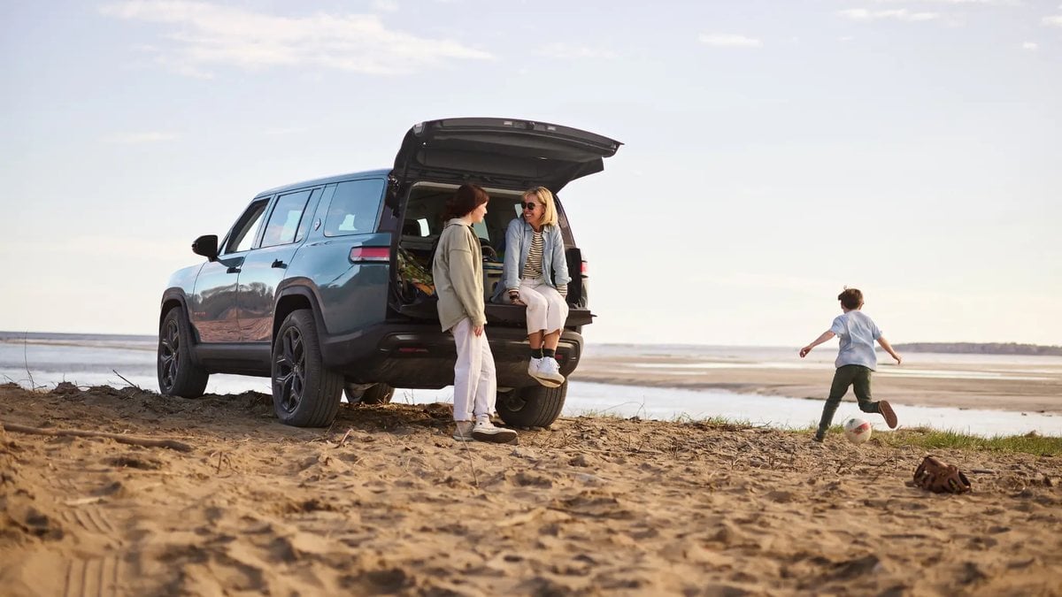 Family spending time at the beach with the rear hatch open of an electric SUV, highlighting road-trip and outdoor lifestyle.