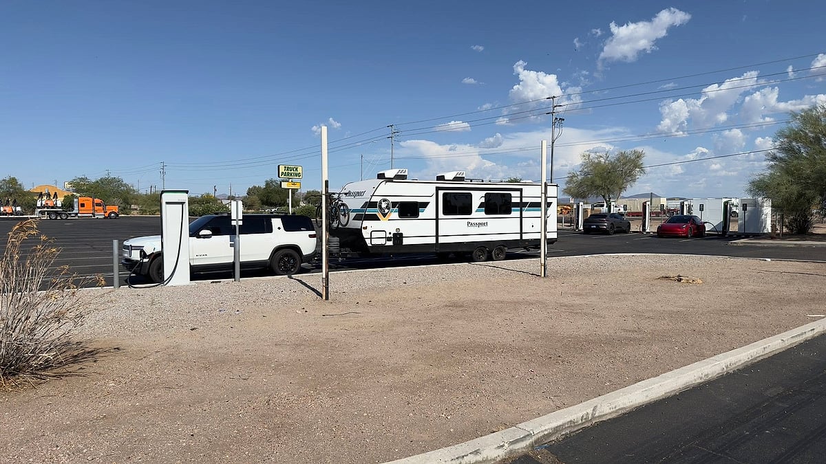 White Rivian R1S and Passport travel trailer shown in side profile at an EV charging station.