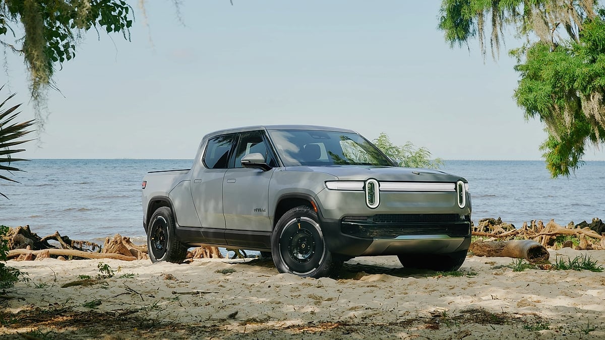 Rivian R1T electric pickup parked on sandy beach with ocean background