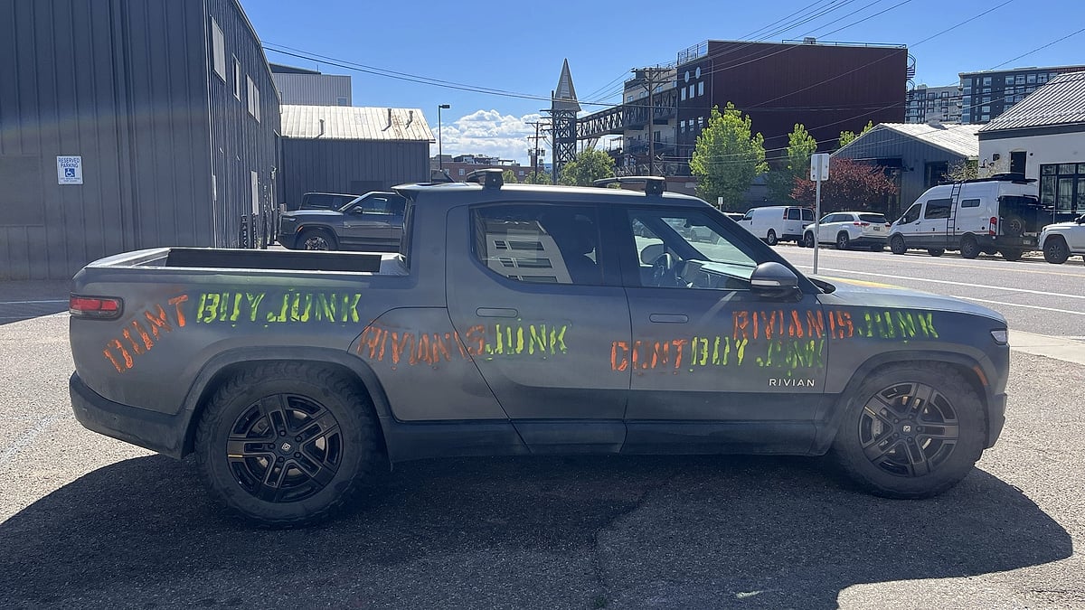 Gray Rivian R1T parked in an urban lot with orange and green graffiti painted across the doors and bed.