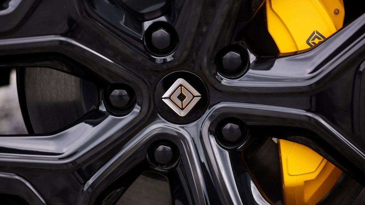 Close-up of a Rivian wheel with glossy black rim and yellow brake caliper, showing performance brake details and center cap.