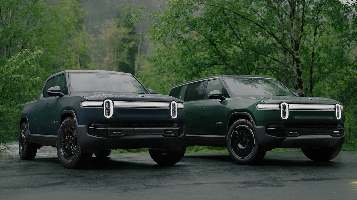 Rivian R1T pickup and R1S SUV parked in a rainy forest setting in a front three-quarter view.