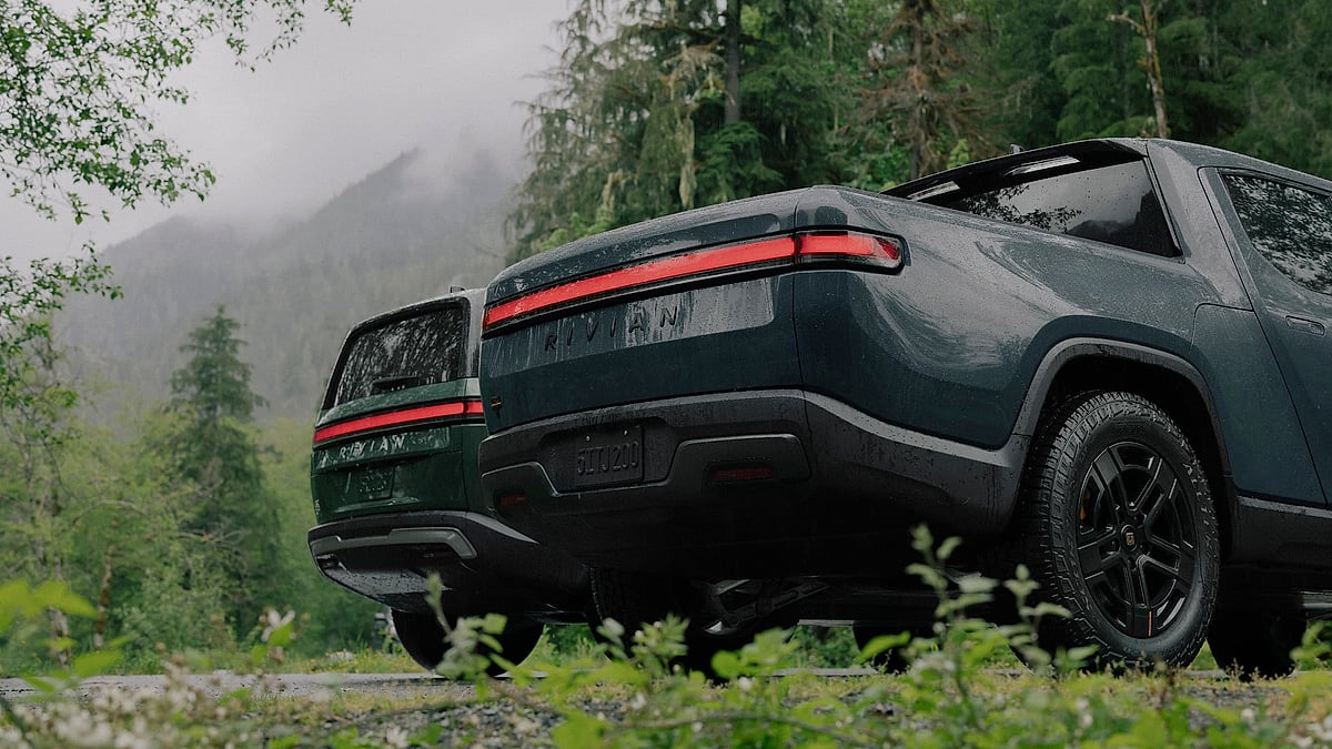Rear view of Rivian R1T and R1S electric vehicles parked in a misty forest landscape.