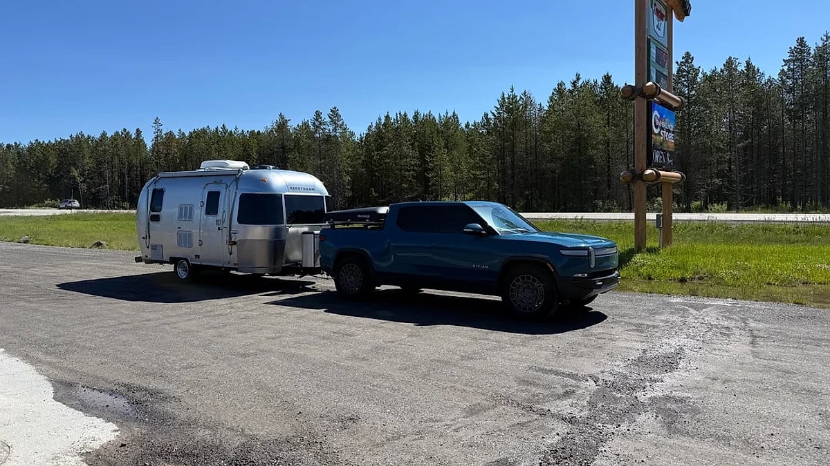 Blue Rivian R1T towing an Airstream travel trailer parked near a roadside travel stop sign.
